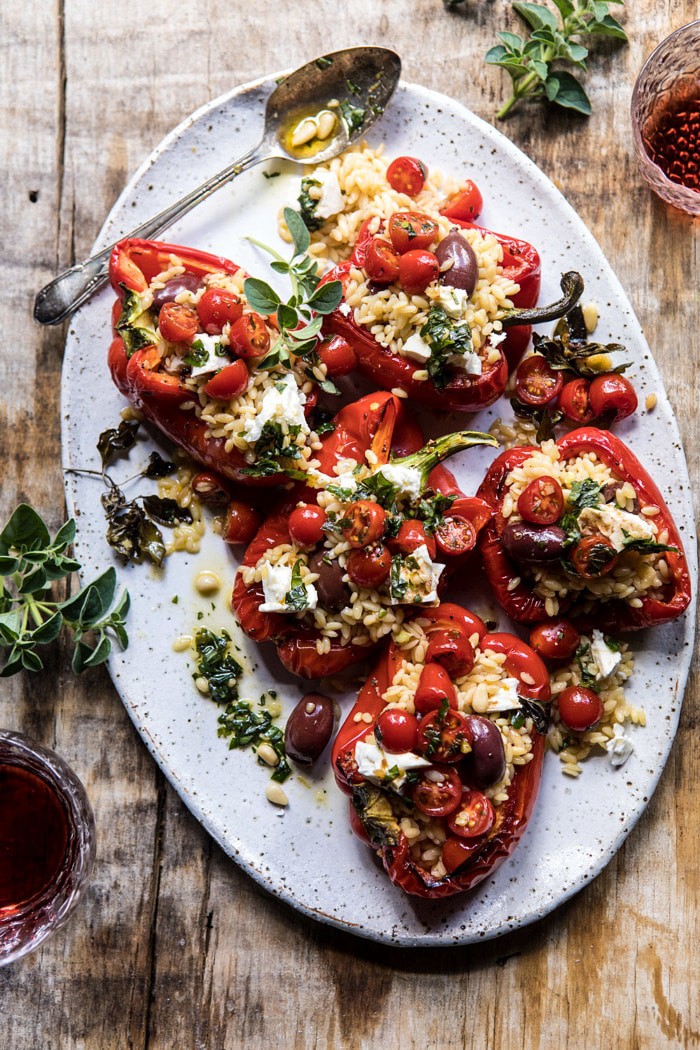 overhead photo of Greek Orzo Stuffed Red Peppers with Lemony Basil Tomatoes, spoon on plates and wine glasses in photo