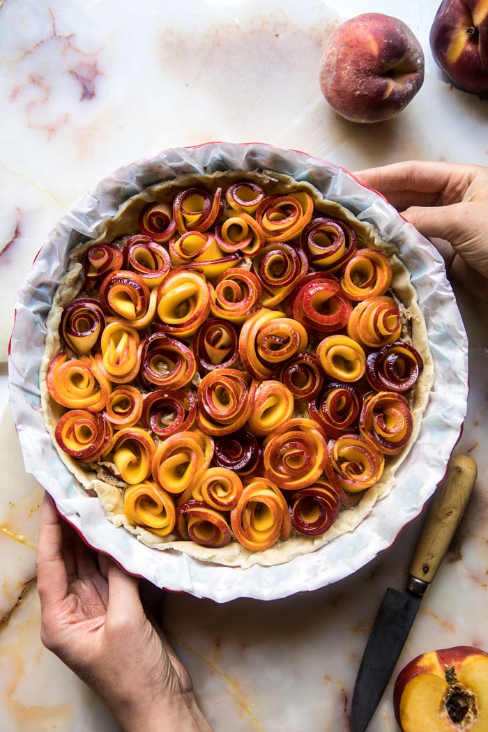 overhead photo of raw Sweet Peach Rose Tart with hands in photo before baking