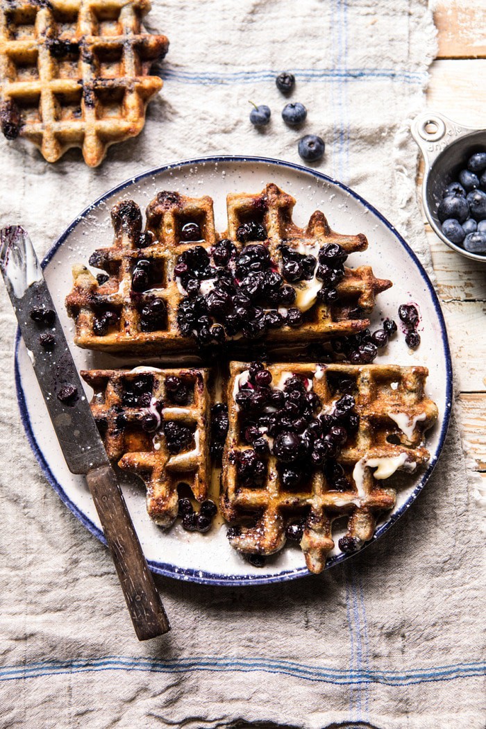 overhead photo of Bursting Blueberry Cornmeal Waffles with butter knife and fresh blueberries in photo 