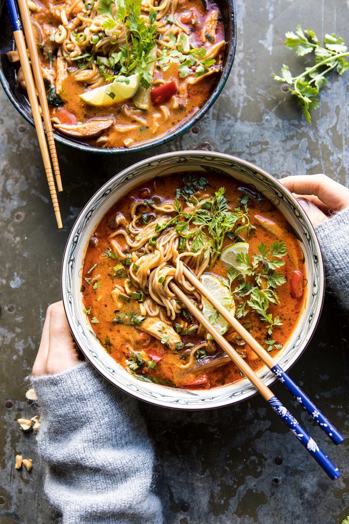 overhead photo of 30 Minute Thai Peanut Chicken Ramen with hands on soup bowl