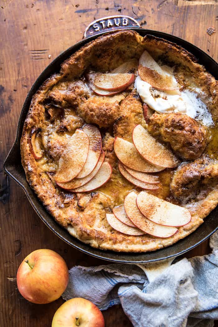 overhead photo of Cinnamon Apple Puffed Pancake in skillet with 2 apples next to it