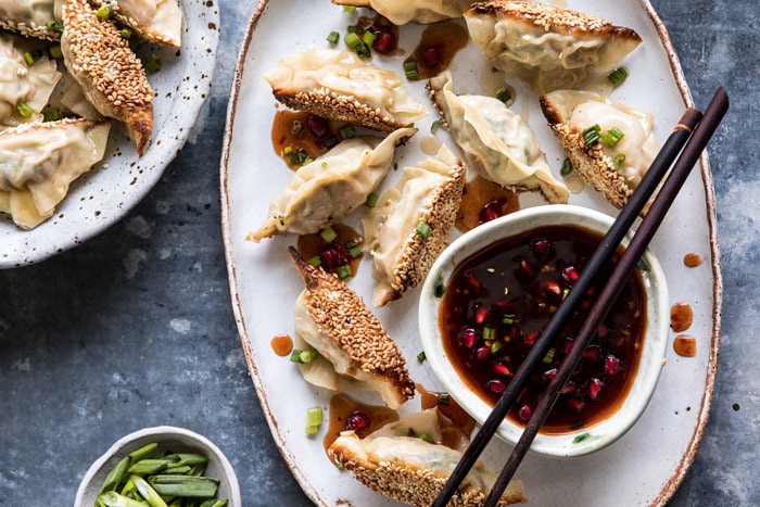 horizontal photo of Ginger Sesame Chicken Potstickers with Sweet Chili Pomegranate Sauce on plate with chopsticks 