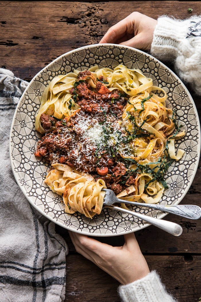 overhead photo of Slow Cooker Vodka Bolognese Pasta with hands on bowl 