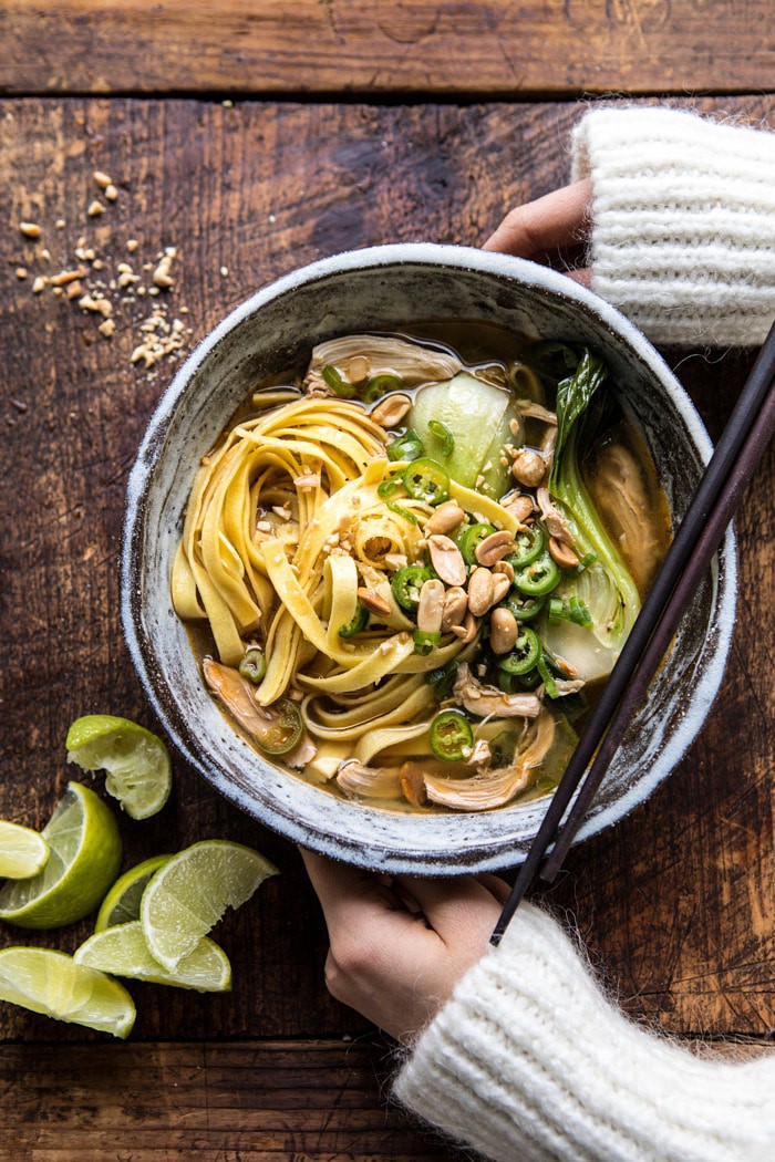 overhead photo of Ginger Peanut Chicken Noodle Soup with hands on bowl