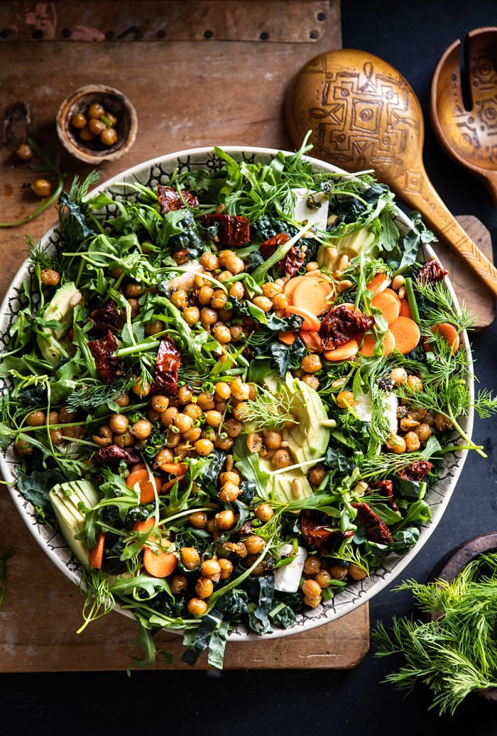 overhead photo of Super Green Sun-Dried Tomato Herb Salad with Crispy Chickpeas with salad spoons and fresh herbs in photo