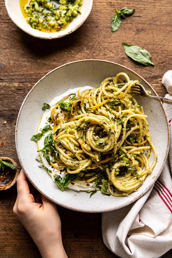 overhead photo of Broccoli Pesto Pasta with Whipped Ricotta and hands on bowl 