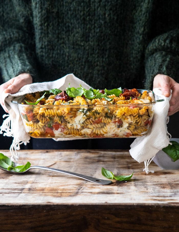 front on photo of Caprese Pesto Pasta Bake with person holding baking dish