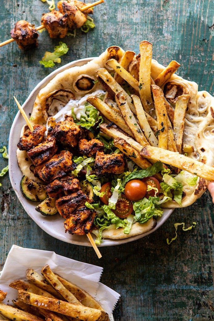 overhead photo of Chicken Souvlaki Bowls with Garlic Fries and chicken off of stick in bowl 