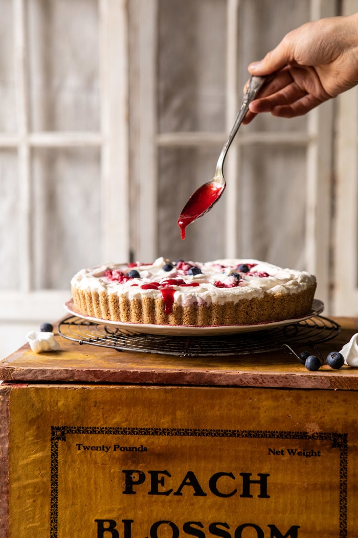 head on photo of No-Bake Eton Mess Berry Cheesecake with raspberry sauce being drizzled over cake