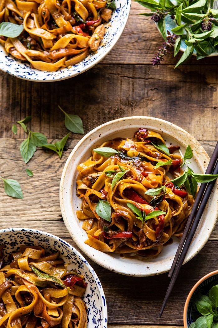 overhead photo of Better Than Takeout Thai Drunken Noodles with chopstick resting on bowl and basil on wood surface