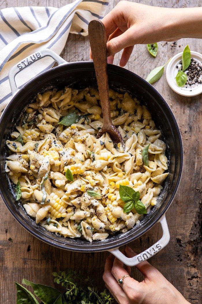 overhead photo of One Pot Lemon Basil, Corn, and Ricotta Pasta with hands on pot and wooden spoon in pot 
