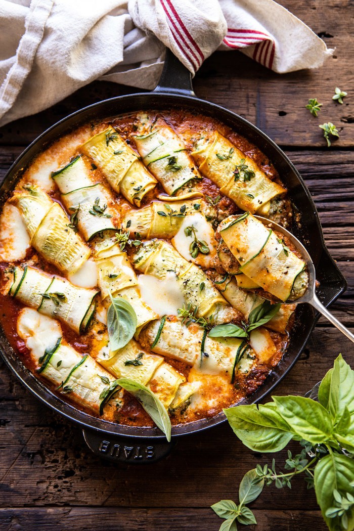 overhead photo of Spicy Pesto and Cheese Stuffed Zucchini Involtini with spoon remove zucchini from baking dish