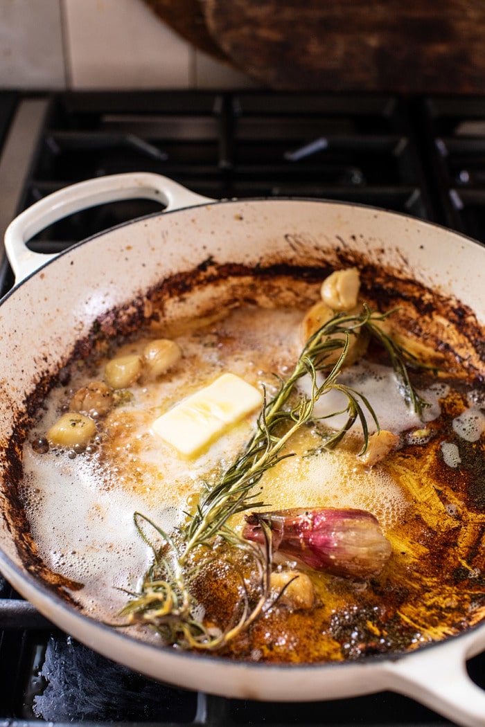 side angled photo of butter, garlic, shallots, and rosemary in skillet on stove