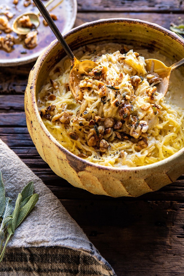 side angled photo of Creamed Spaghetti Squash with Browned Butter Walnuts with hands pulling up the spaghetti squash 