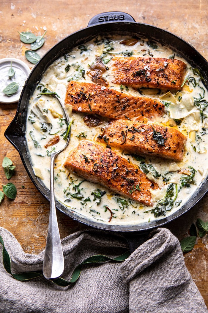 overhead photo of Creamy Spinach and Artichoke Salmon in skillet with spoon in sauce