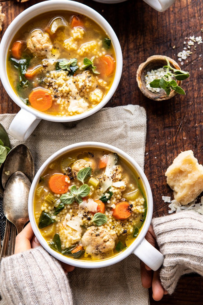 overhead photo of Healthier Italian Wedding Soup with Lemon and Garlic with hand on soup bowl