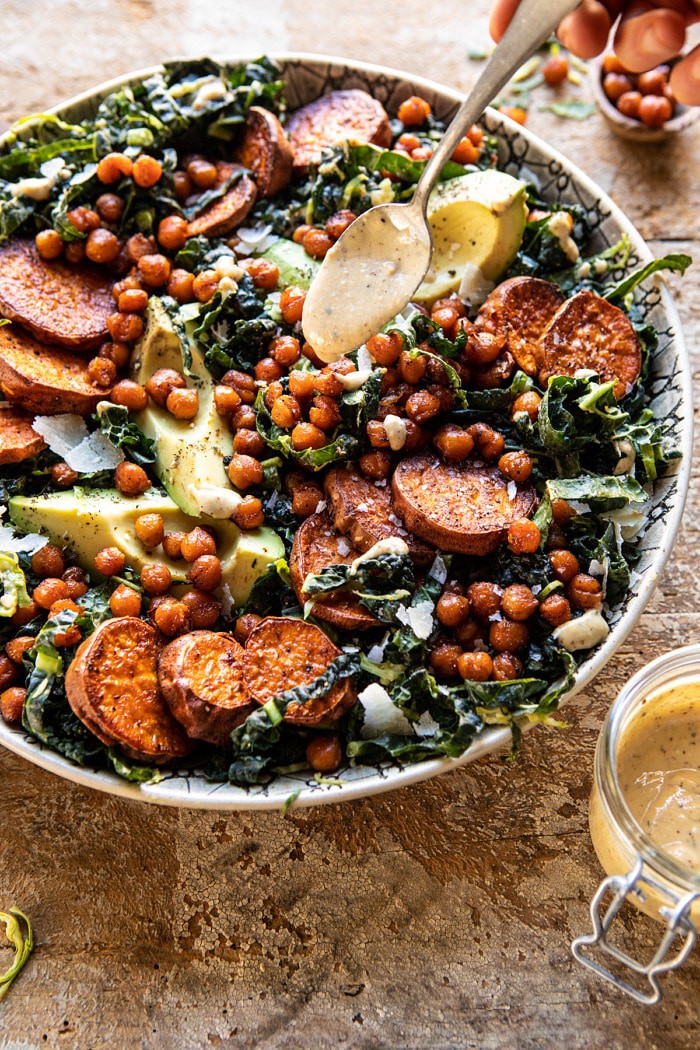 side angled photo of Kale Caesar Salad with Sweet Potatoes and Crispy Chickpeas with spoon drizzling dressing over salad
