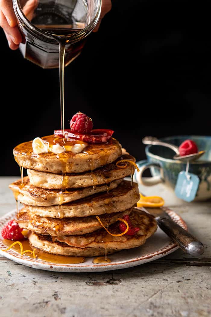 side angled photo of Earl Grey Lemon Ricotta Pancakes with Salted Maple Butter and maple syrup being drizzled over pancakes
