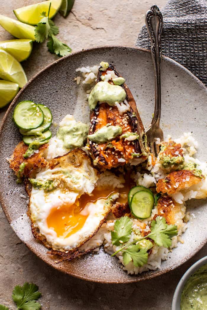 overhead photo of Crispy Rice Bowl with Browned Butter Sweet Potatoes and Herby Green Tahini with fork in bowl and fried egg broken to expose the yolk