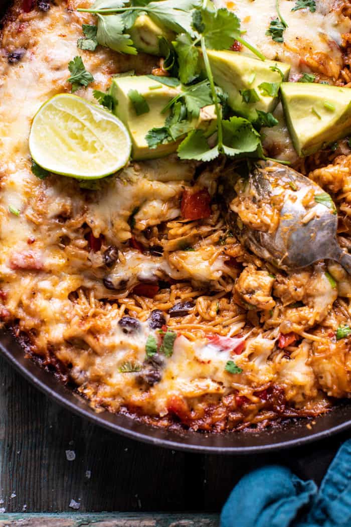 overhead close up photo of One Skillet Cheesy Cuban Chicken Rice Bake with cheese melted and spoon in skillet pulling up the cheese
