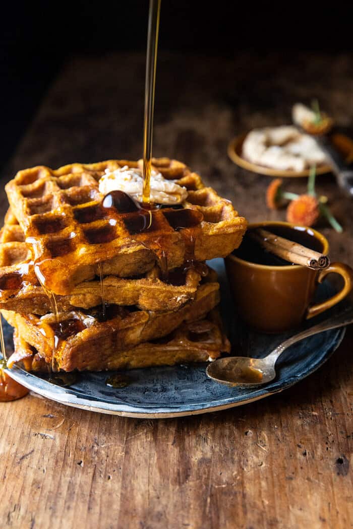 side angled action photo of Cider Pumpkin Waffles with Salted Maple Butter (the maple is being poured on the waffles)