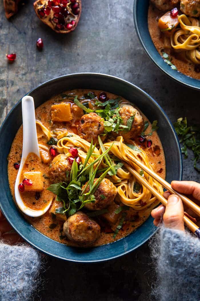 overhead photo of Creamy Coconut Chicken Meatball and Noodle Curry with hands on bowl 